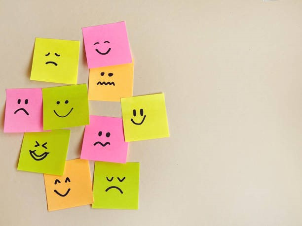 Sticky notes aan een muur met gezichtjes erop getekend met verschillende emoties.