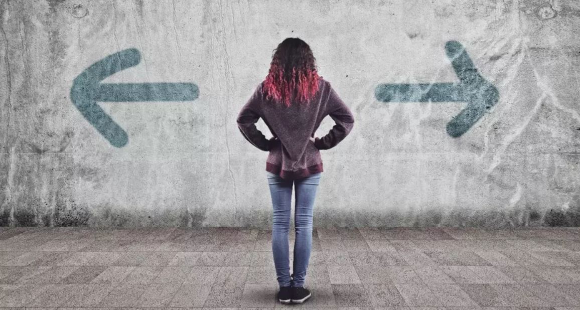 Een vrouw staat met haar gezicht naar de muur. Op de muur een pijl naar links en naar rechts